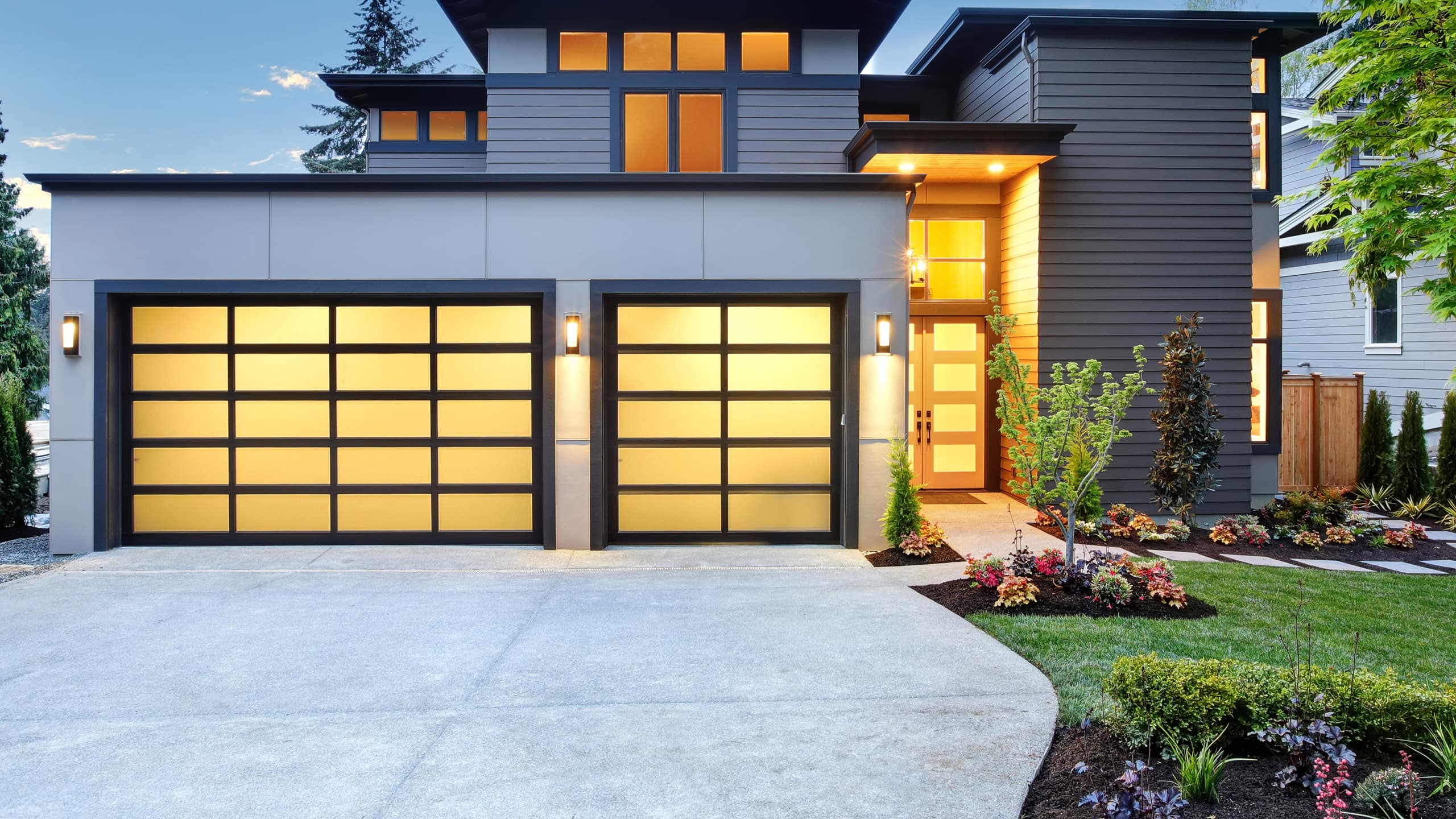 A contemporary, suburban home with a full-view double car and single car garage door at dusk