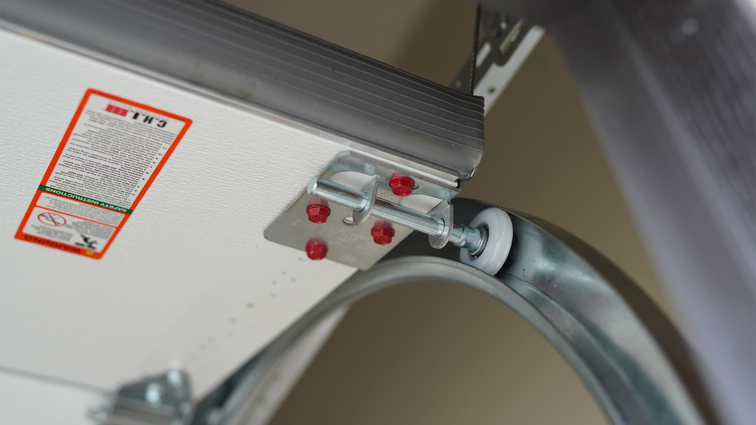 Close-up of a white C.H.I. garage door installed by PDQ Doors with roller wheels in the garage door track with the garage door hinges in view