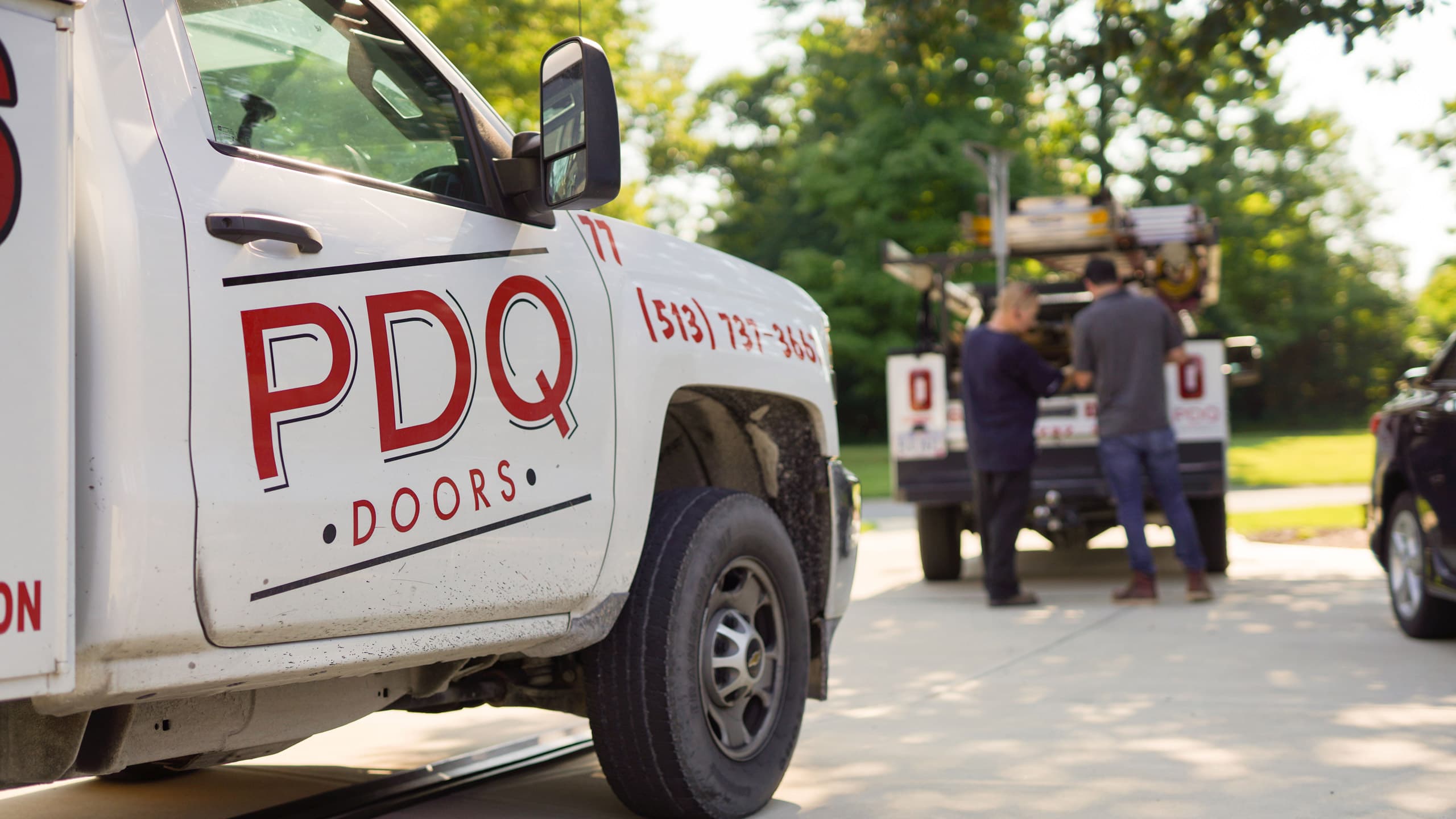 PDQ Doors service, installation, and repair trucks parked in a driveway on a sunny day with technicians in the background