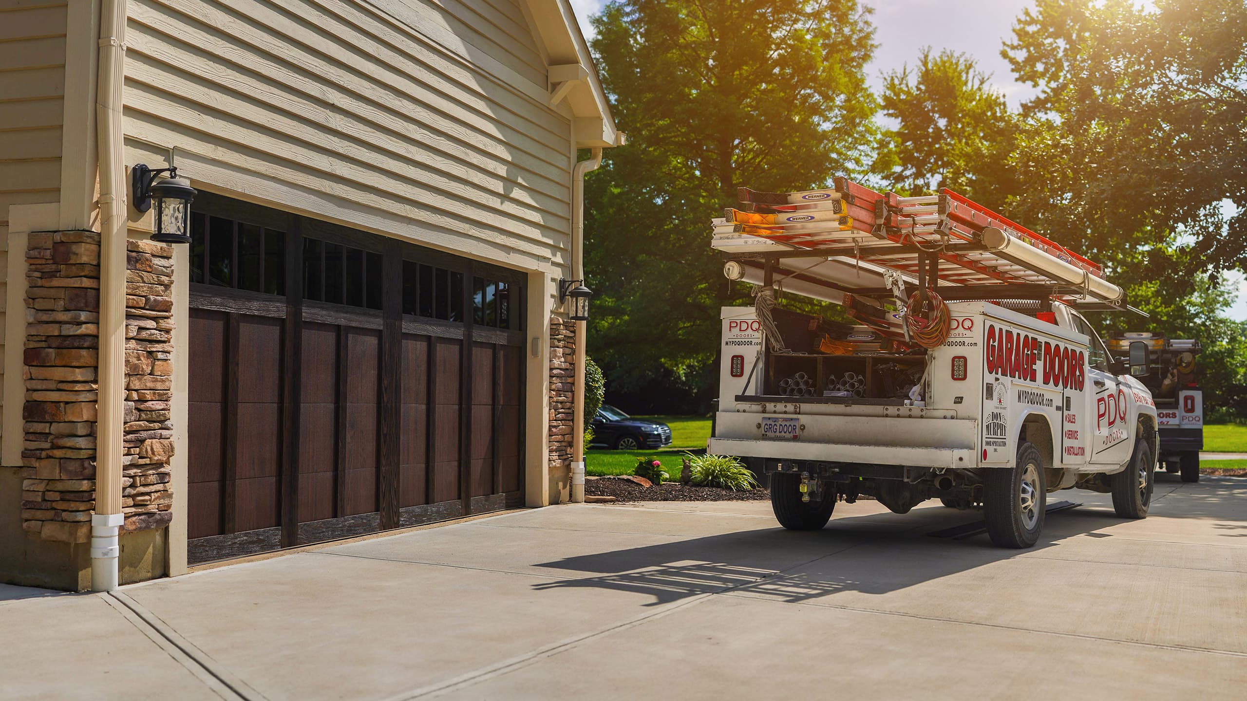 PDQ Doors service and installation truck parked on a driveway next to newly installed garage door on a residential home on a sunny day