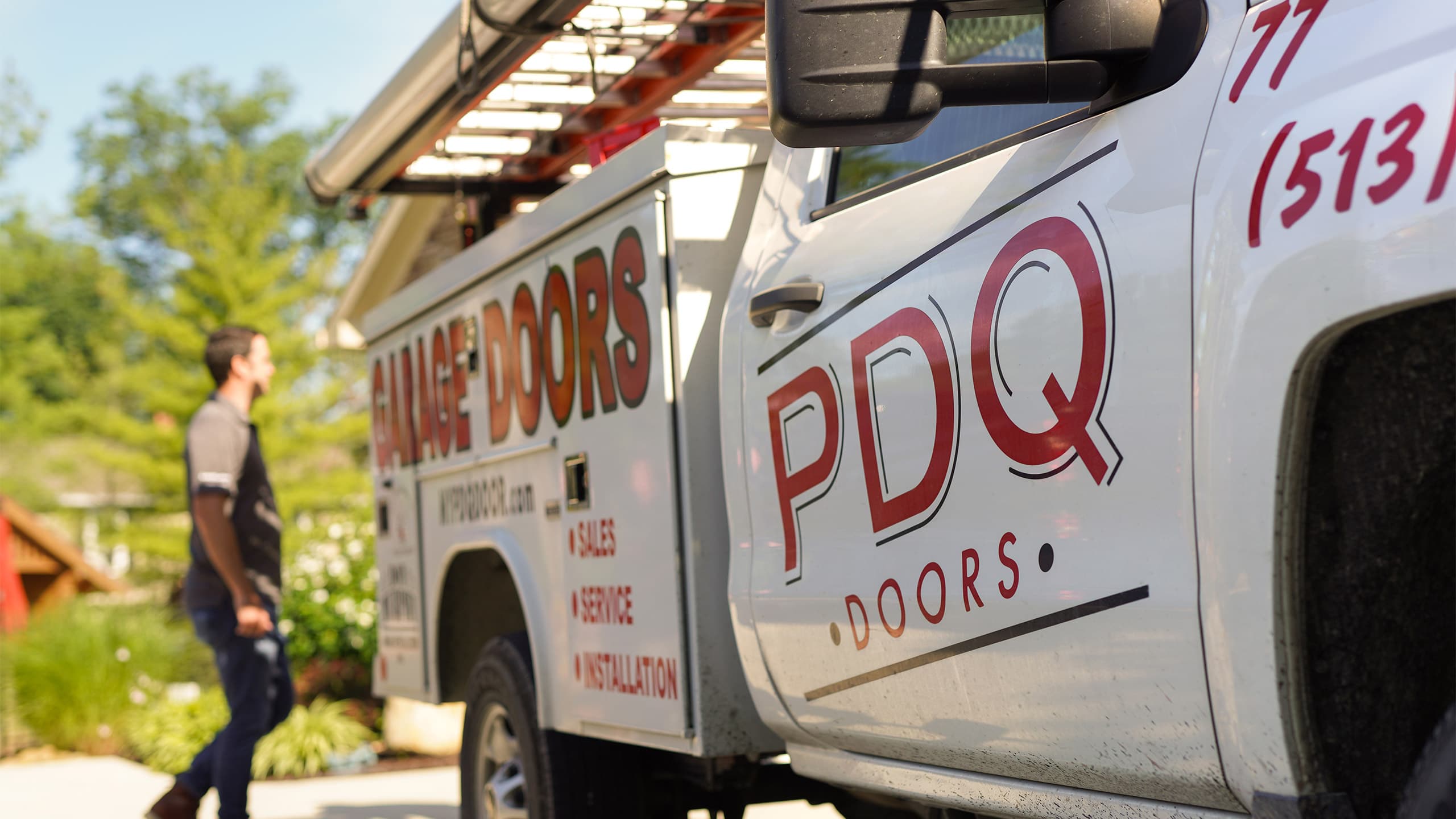 A white PDQ Doors service and installation truck parked in a driveway with a PDQ Doors technician in the background
