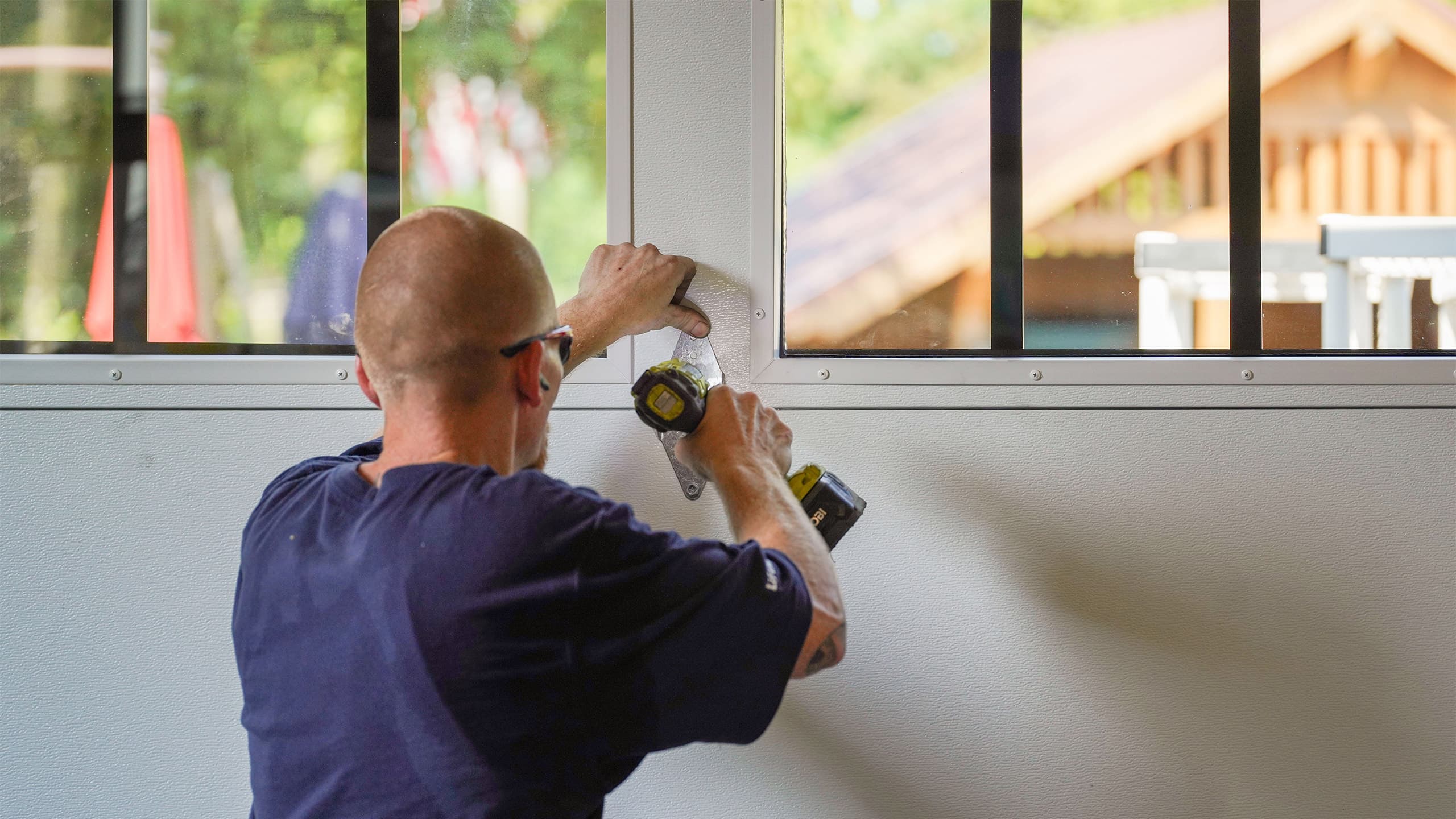 A PDQ Doors technician repairs a garage door hinge on a white garage door with windows