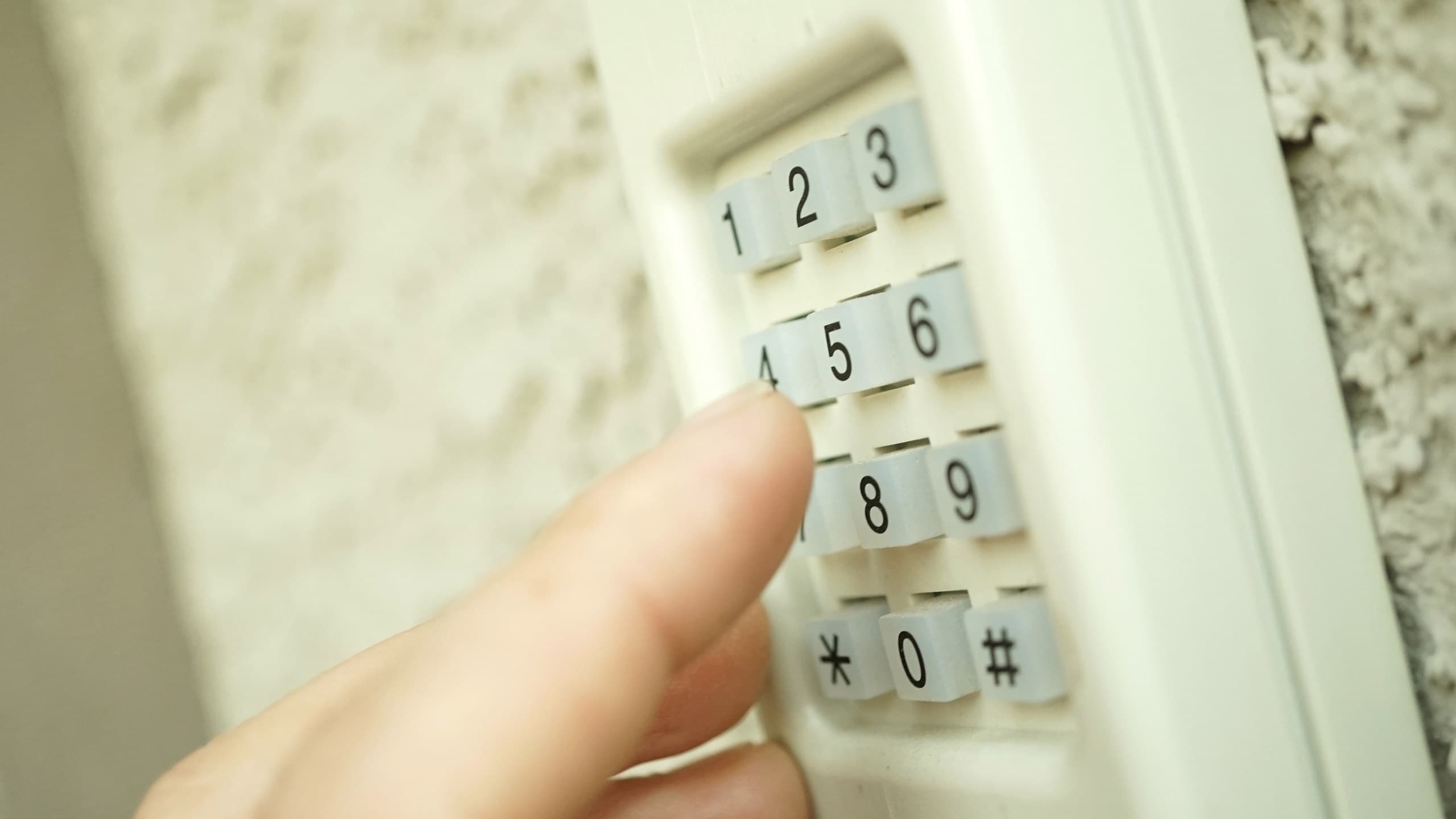 Close-up of a person pressing buttons on a beige exterior garage door keyless entry keypad