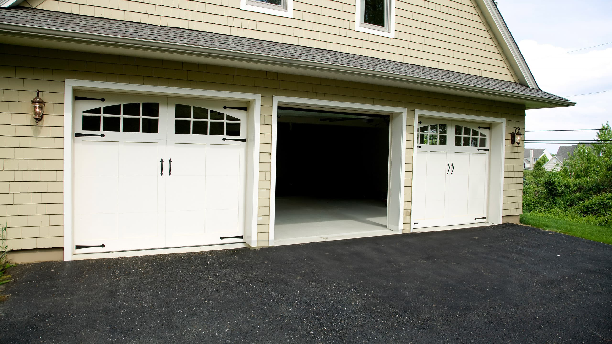 A tan suburban home with three white single car carriage house garage doors, middle door opened