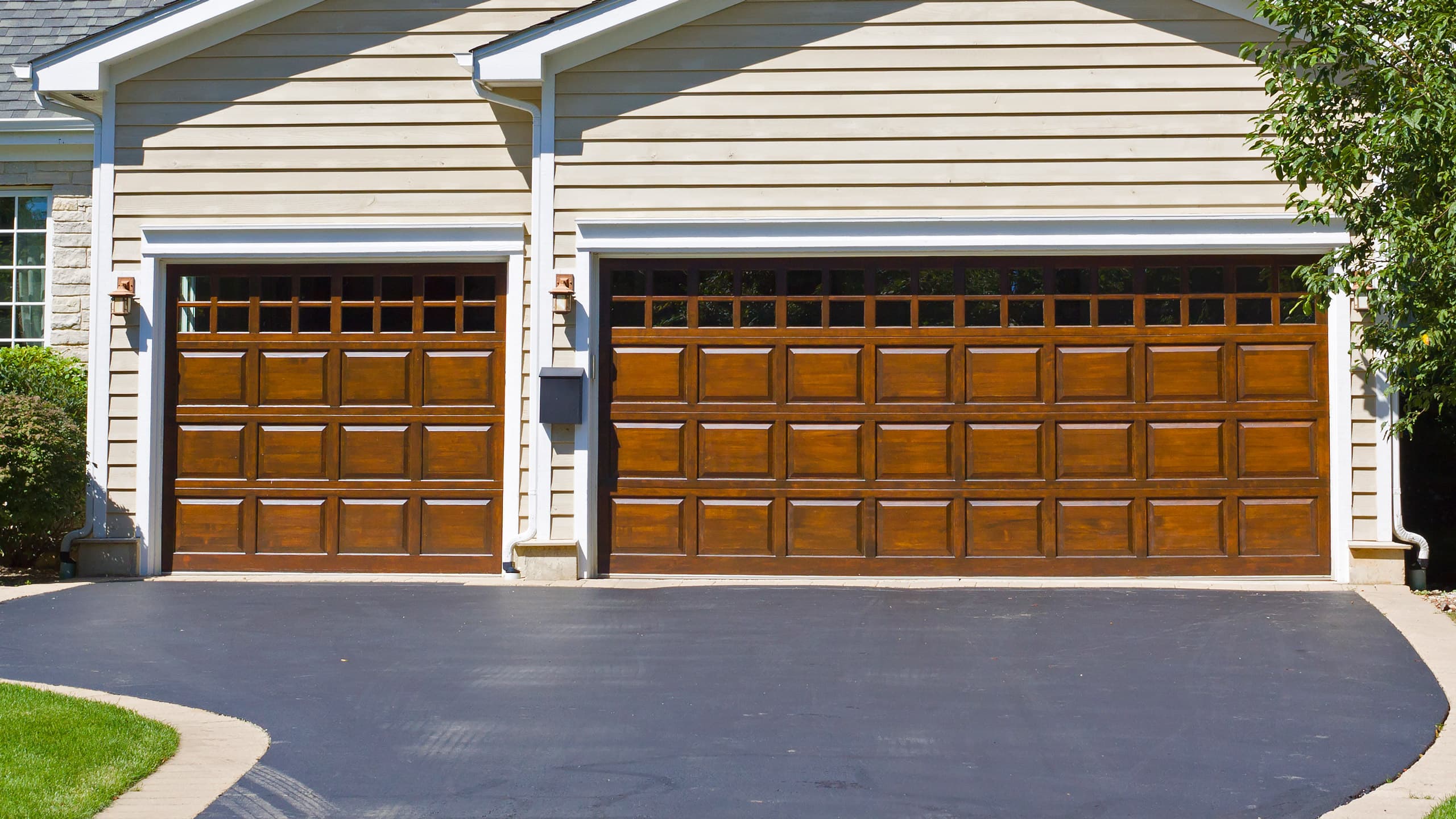 A suburban home with a wooden, traditional style garage door and blacktop driveway on a sunny day