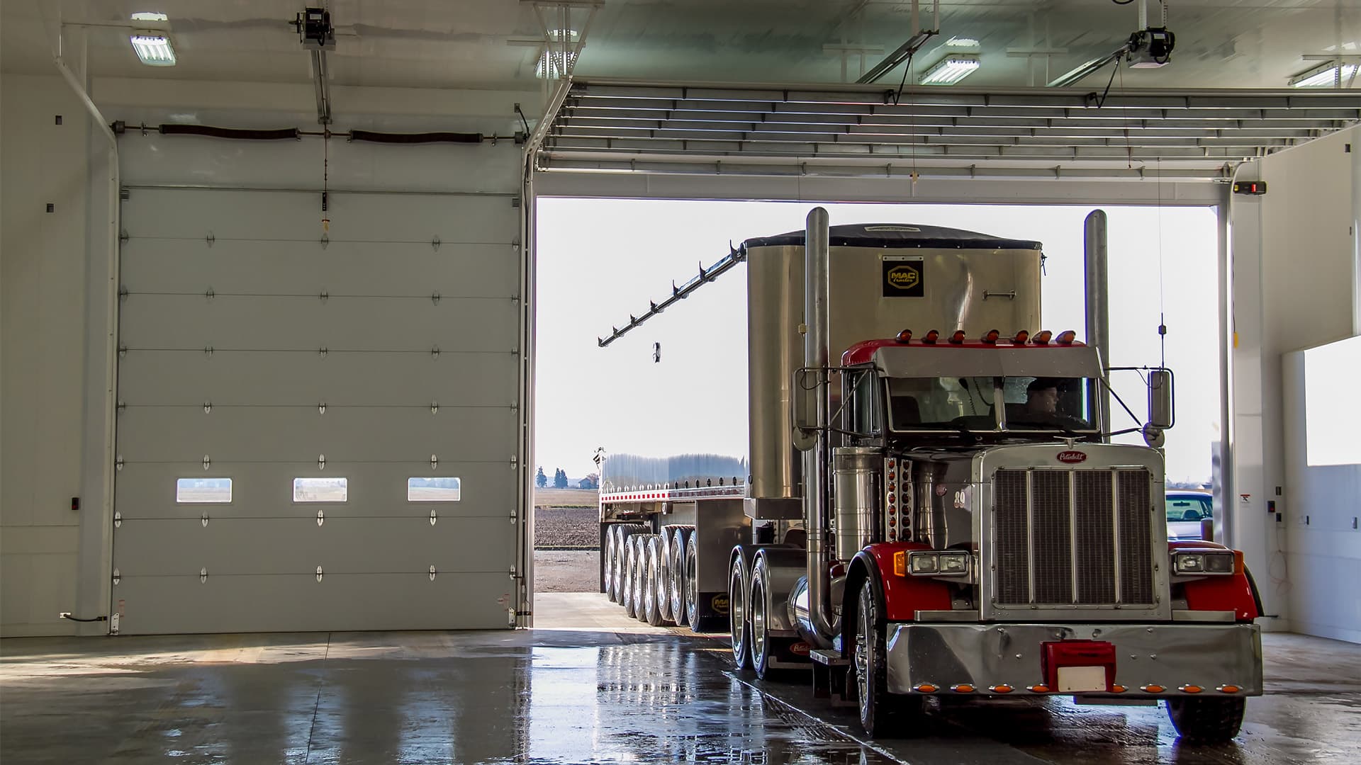 A red commercial tractor trailer truck with a trailer parked in a commercial garage