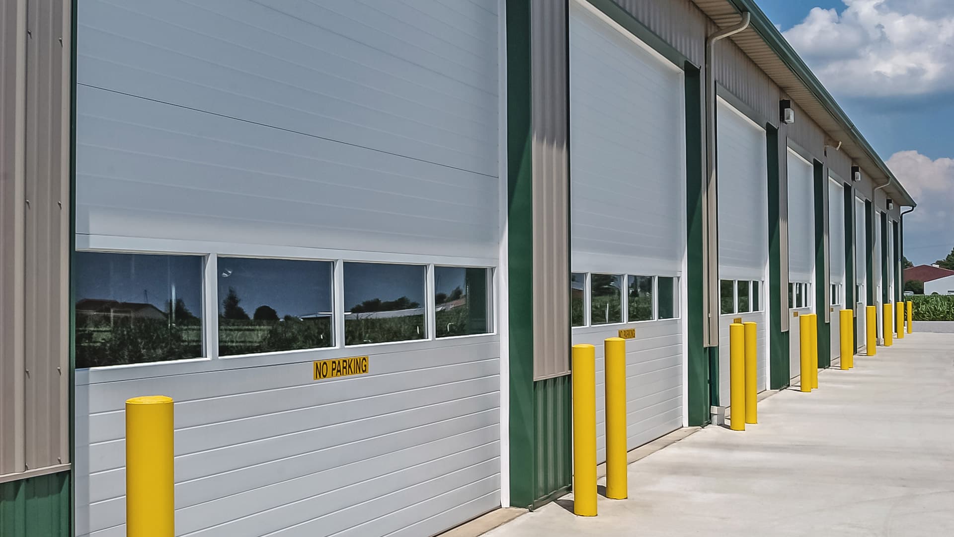 Front of a commercial warehouse building with a row of white commercial polyurethane thermal garage doors with windows in the middle of each